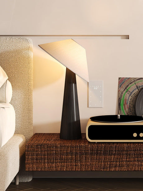 Black tilted shade table lamp lit on a bench beside a record player