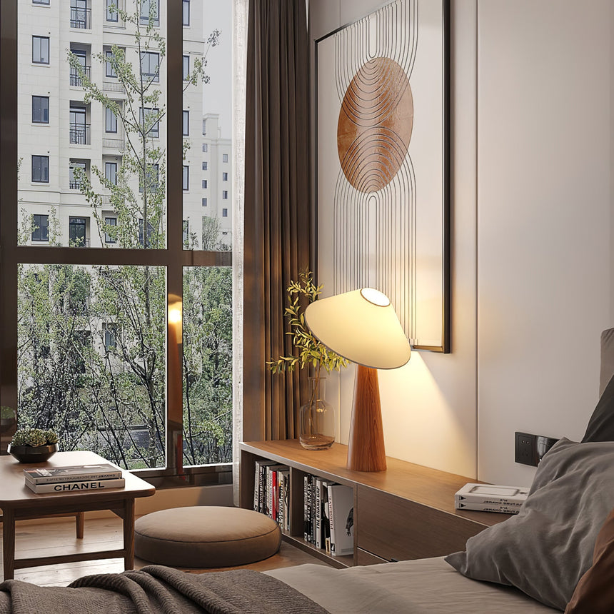 Tilted shade table lamp lit on a low table in a bedroom by a window