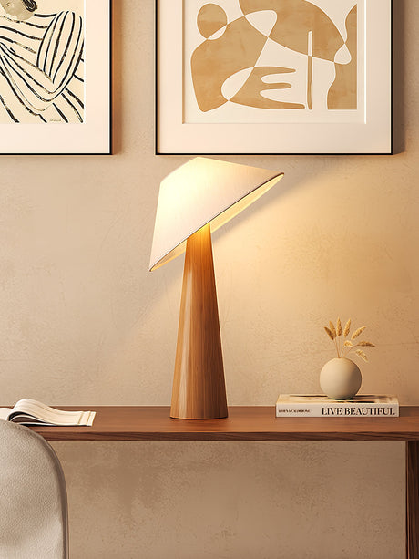 Tilted shade table lamp lit on a sideboard beside a small round vase