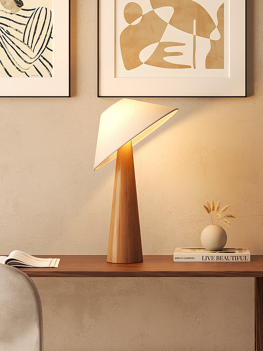 Tilted shade table lamp lit on a sideboard beside a small round vase