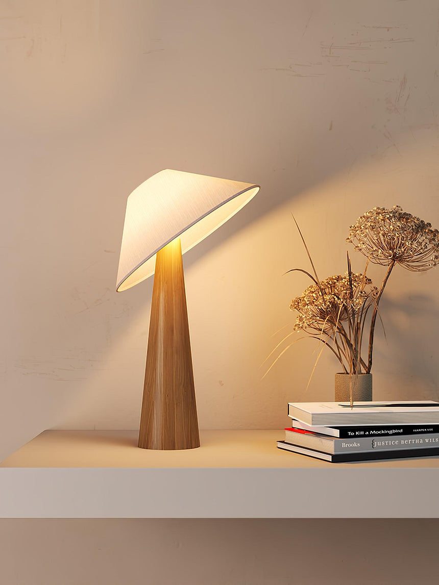 Tilted shade table lamp lit on a shelf beside dried flowers