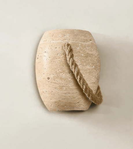 The urn unlit on a cream wall, the travertine pores and the rope loop clear