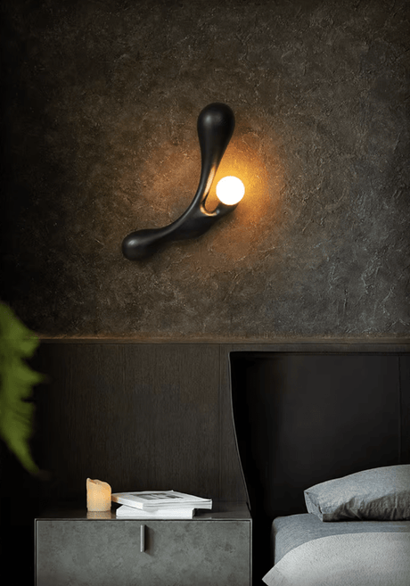 Sconce lit above a low bed beside a tray of ceramics on a dark surface
