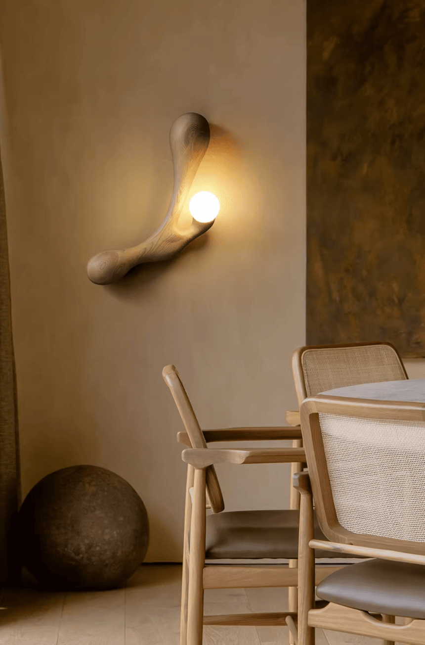 Sconce lit above a dining table with pale wood chairs around it