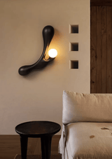 Sconce lit above a pale sofa beside a black stool and a wall panel