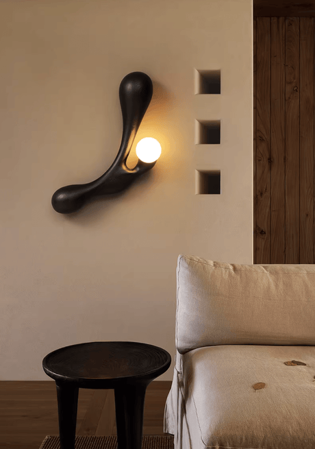 Sconce lit above a pale sofa beside a black stool and a wall panel