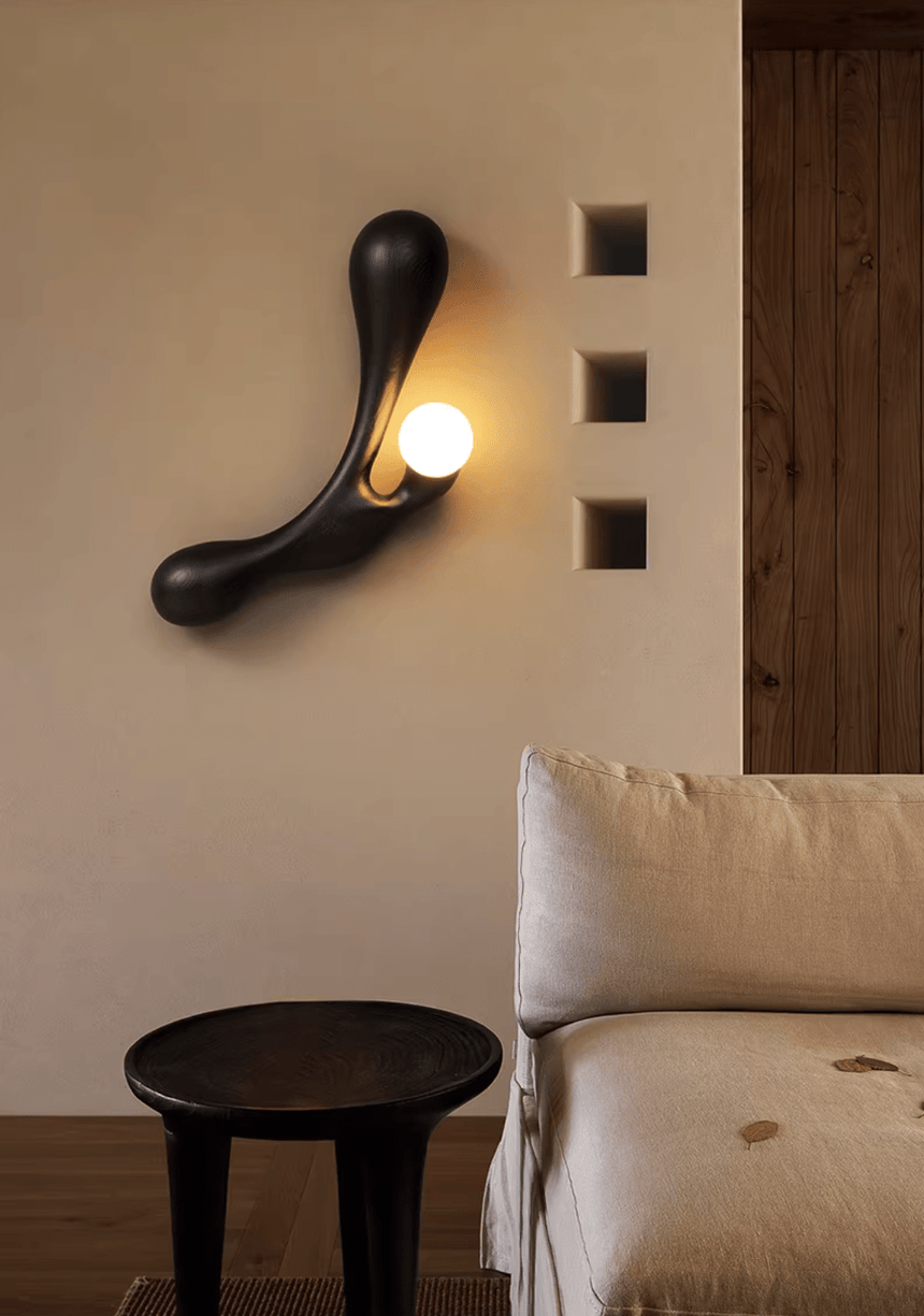 Sconce lit above a pale sofa beside a black stool and a wall panel
