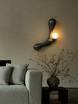 Sconce lit beside a pale sofa and a vase of branches on a side table