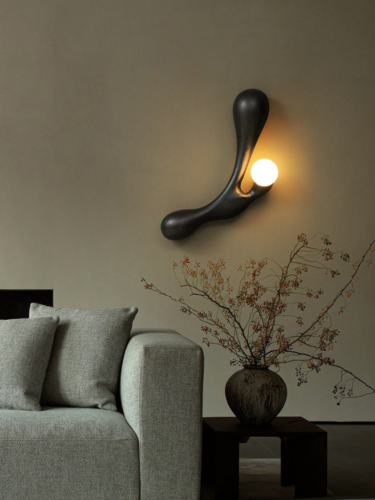 Sconce lit beside a pale sofa and a vase of branches on a side table