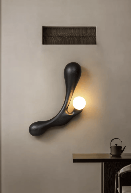 Sconce lit above a dark tea table set with a small pot and a cup