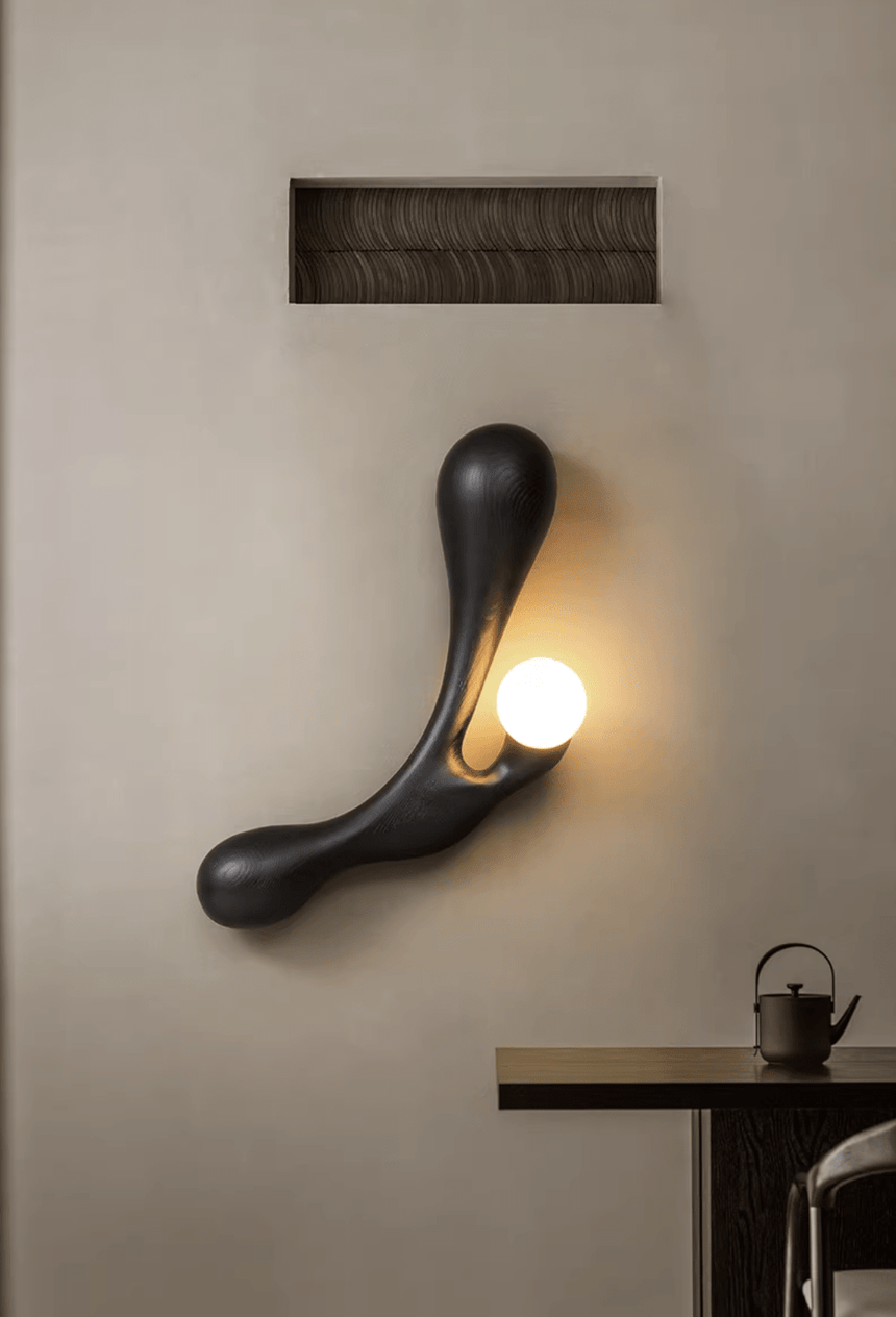 Sconce lit above a dark tea table set with a small pot and a cup