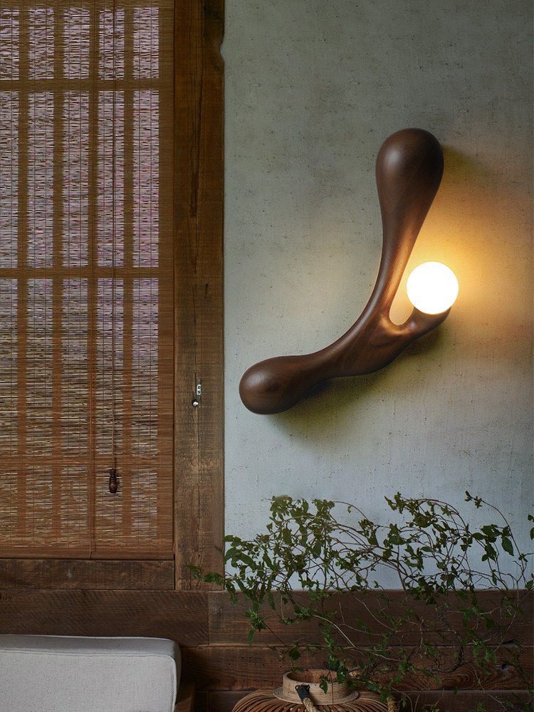 Sconce lit on a plaster wall beside a wood screen and a climbing plant