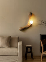 Sconce lit above a pale armchair beside a small dark wooden stool