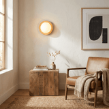 Sconce lit beside an armchair with a throw, a wood cube table and artwork