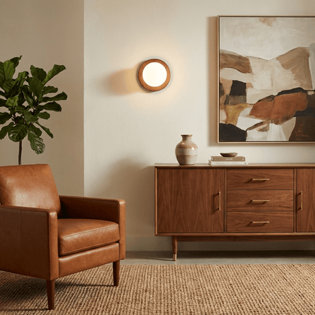 Sconce lit beside framed artwork above a sideboard and a leather armchair