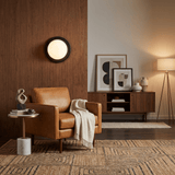 Sconce lit on a wood panel wall beside a leather armchair and a sideboard