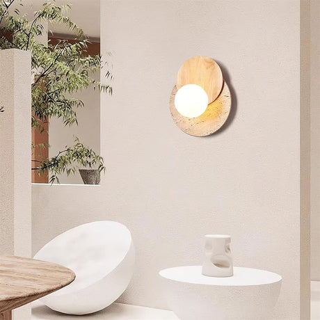 Sconce lit on a plaster wall beside a dining table and stone stools