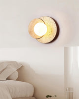 Sconce lit above a bed beside a tall pale column and a plant