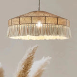 Jute pendant light with a fringed drum shade lit above dried grasses