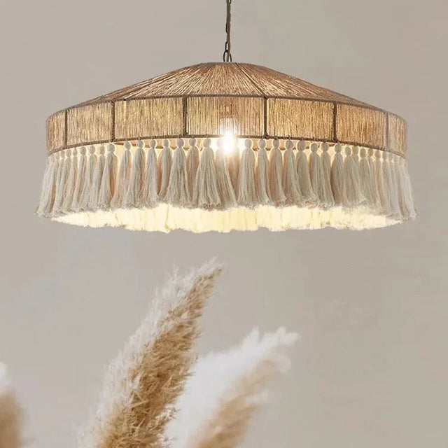 Jute pendant light with a fringed drum shade lit above dried grasses