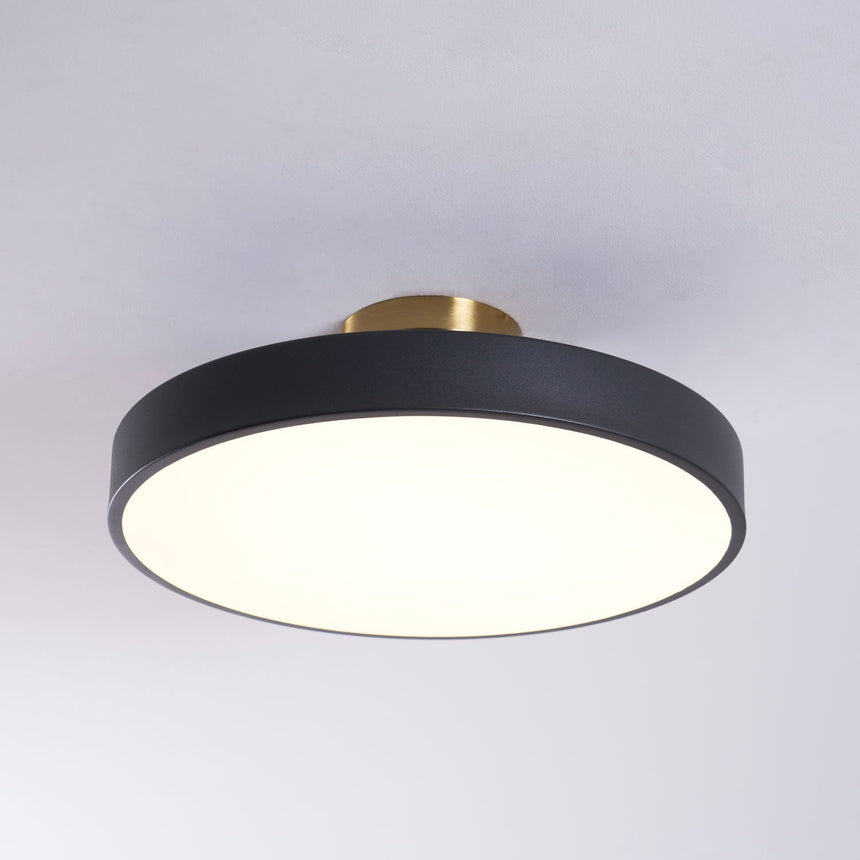 Black drum ceiling light lit against a pale backdrop