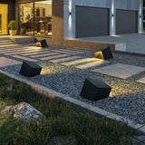 Several lit along a gravel strip and a paved walk beside a garage