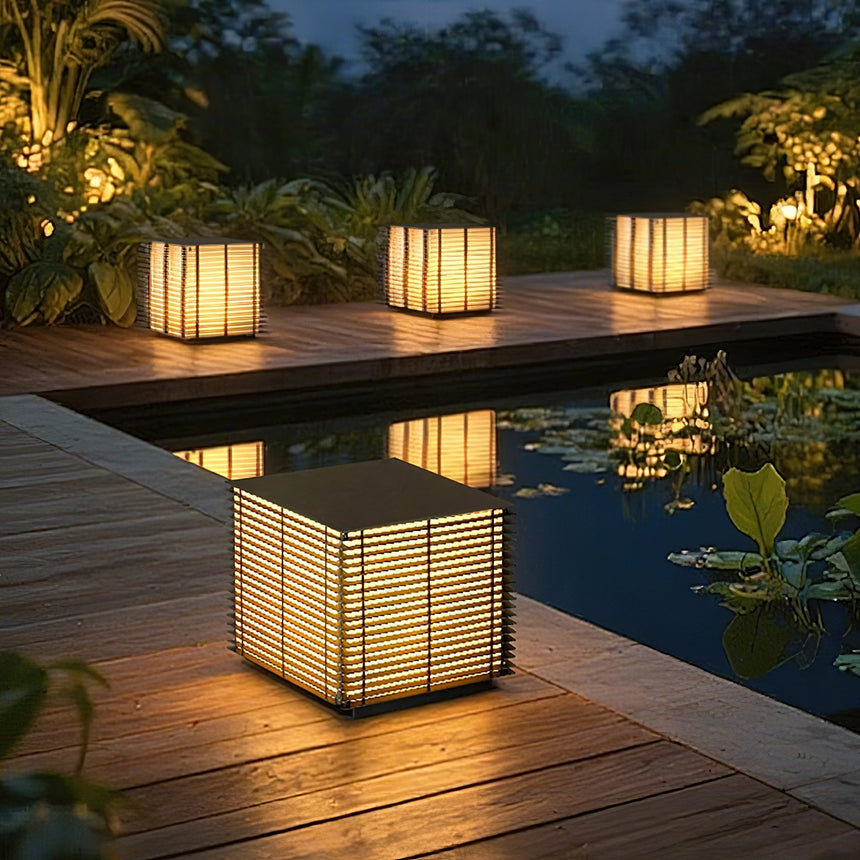 Two louvered cubes lit on a timber deck beside a pool at nightfall