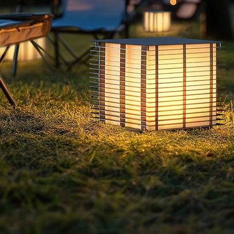 The louvered cube lit low in long grass at the edge of a lawn