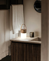 Lantern table lamp lit on a bathroom shelf beside a folded towel