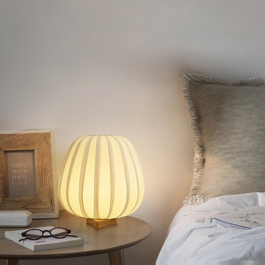 Pleated lantern lamp lit on a nightstand beside a pillow and a frame
