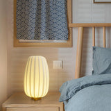 Pleated lantern lamp lit on a bedside table against a wood headboard