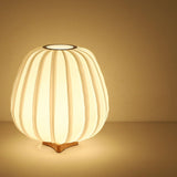 Short pleated lantern lamp lit warm on a plain pale ground