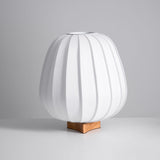 Short round pleated fabric lantern lamp unlit on a wood cross foot
