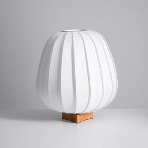 Short round pleated fabric lantern lamp unlit on a wood cross foot