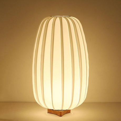 Tall pleated lantern lamp lit warm, the ribs glowing from inside