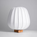 Tall pleated fabric lantern lamp unlit on a small wood cross foot