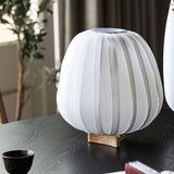 Pleated lantern lamp lit on a dark table beside a cup and books