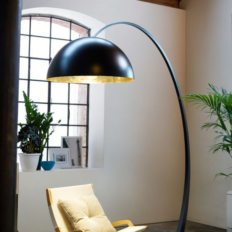 The black lamp lit over a wooden armchair beside a tall window and two plants