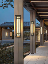 Lanterns lit along a colonnade walk beside clipped shrubs at dusk