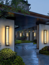 The lantern lit in a courtyard with pines and a lit soffit behind it