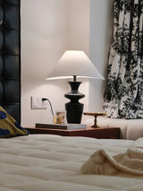 Large table lamp lit in a bedroom at night beside a dark headboard