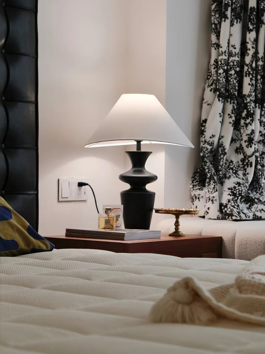 Large table lamp lit in a bedroom at night beside a dark headboard