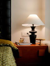 Large table lamp lit on a wooden chest beside a bed with a green blanket