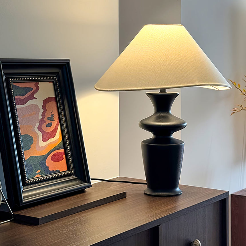 Large table lamp lit on a console beside a framed print in a pale room