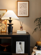 Large table lamp lit on a dark shelf unit beside books and a diffuser