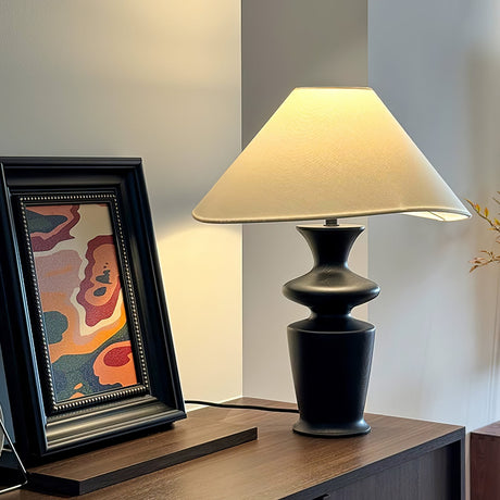 Large table lamp lit on a wooden desk beside an open book and fruit