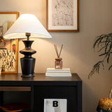Large table lamp lit on a dark desk beside books and a framed picture