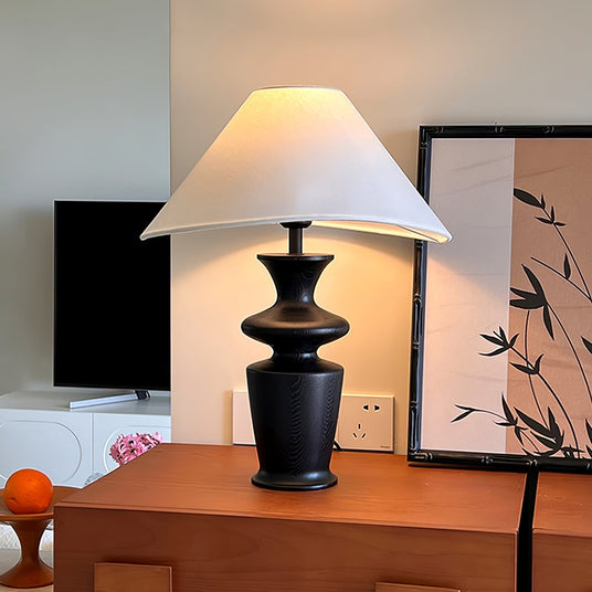 Large table lamp lit on a wooden chest beside a television and framed prints