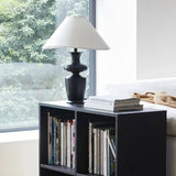 Large table lamp standing on a low bookcase in front of a bright window