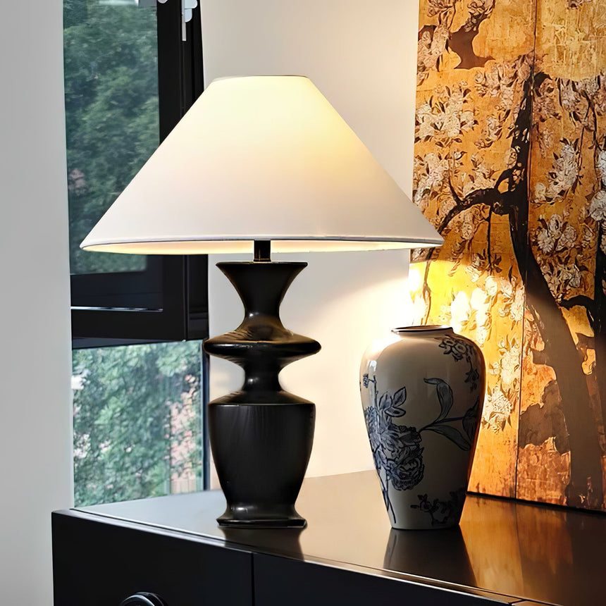 Large table lamp on a dark chest at a window beside a painted vase